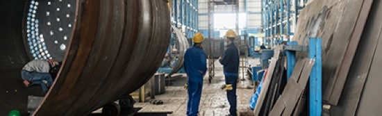 Two workers in a factory wearing hard hats.