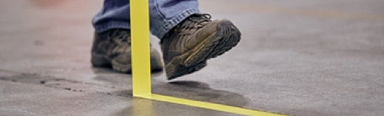 A person's feet, walking beside tape that is being pulled off of a floor.